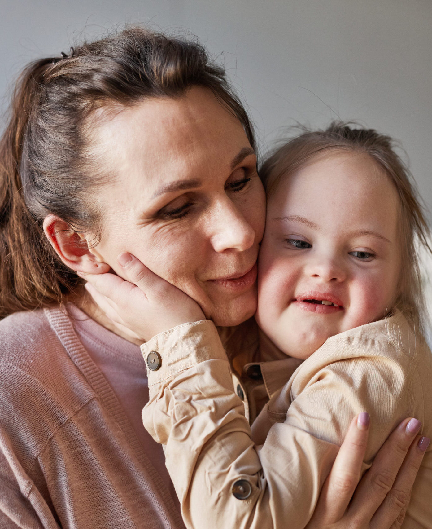 Candid portrait of cute girl with down syndrome hugging mother lovingly in simple home interior, copy space